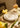 Sebuah meja makan yang ditata dengan piring putih dan peralatan makan bergaya rumah eropa di atas taplak meja bertekstur dengan nada emas. Meja ini dihiasi penuh dengan bunga kertas bernuansa kuning.