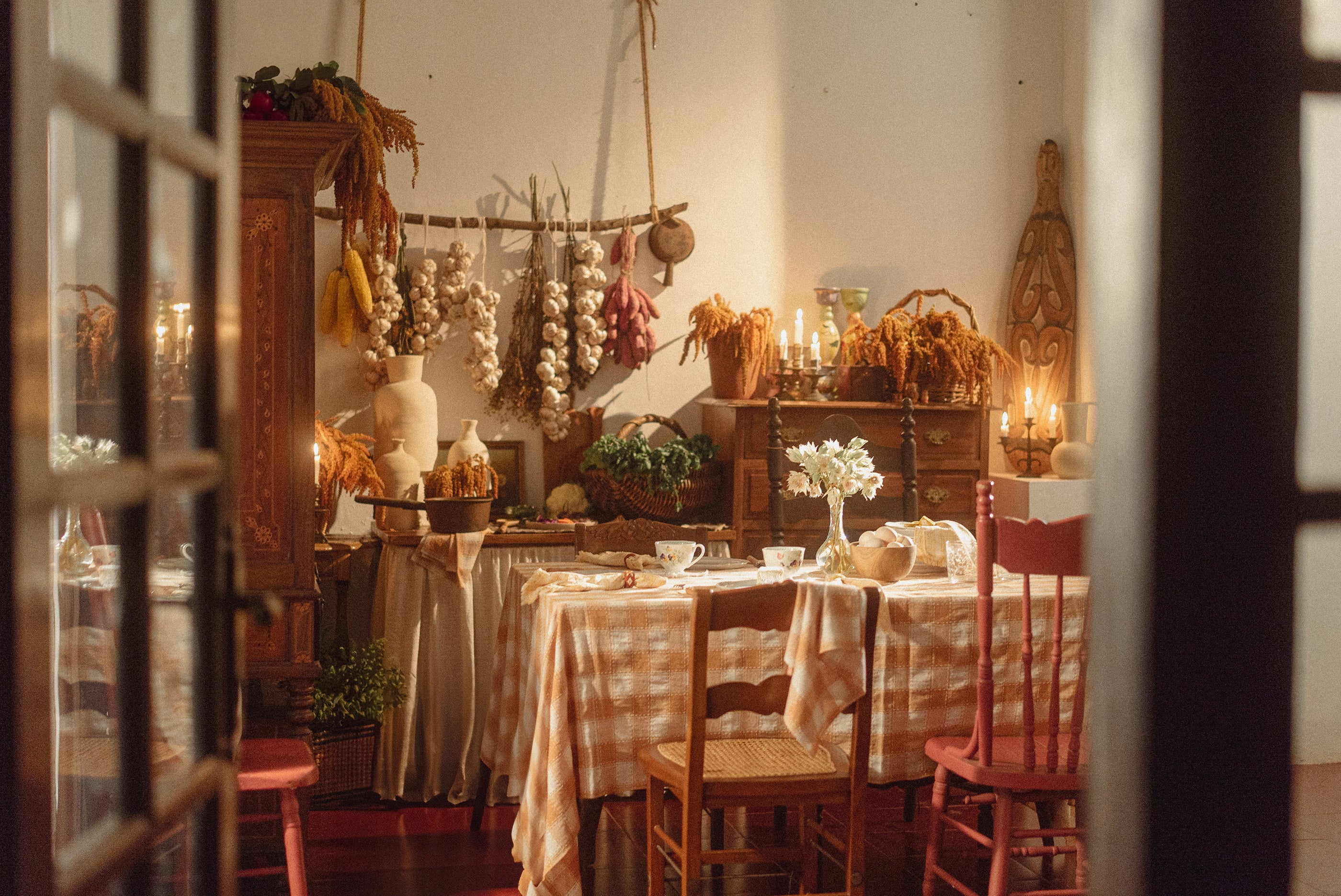 Suasana dapur klasik dengan bunga kering menghiasi dinding, dilengkapi dengan meja makan yang dihiasi taplak meja kotak-kotak berwarna pink.